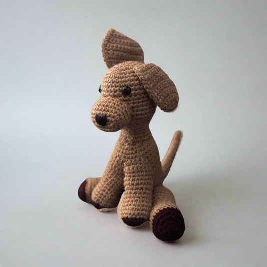 Brown hand crocheted dog sitting with the hind paws spread out and the front paws placed in front with the tail upright