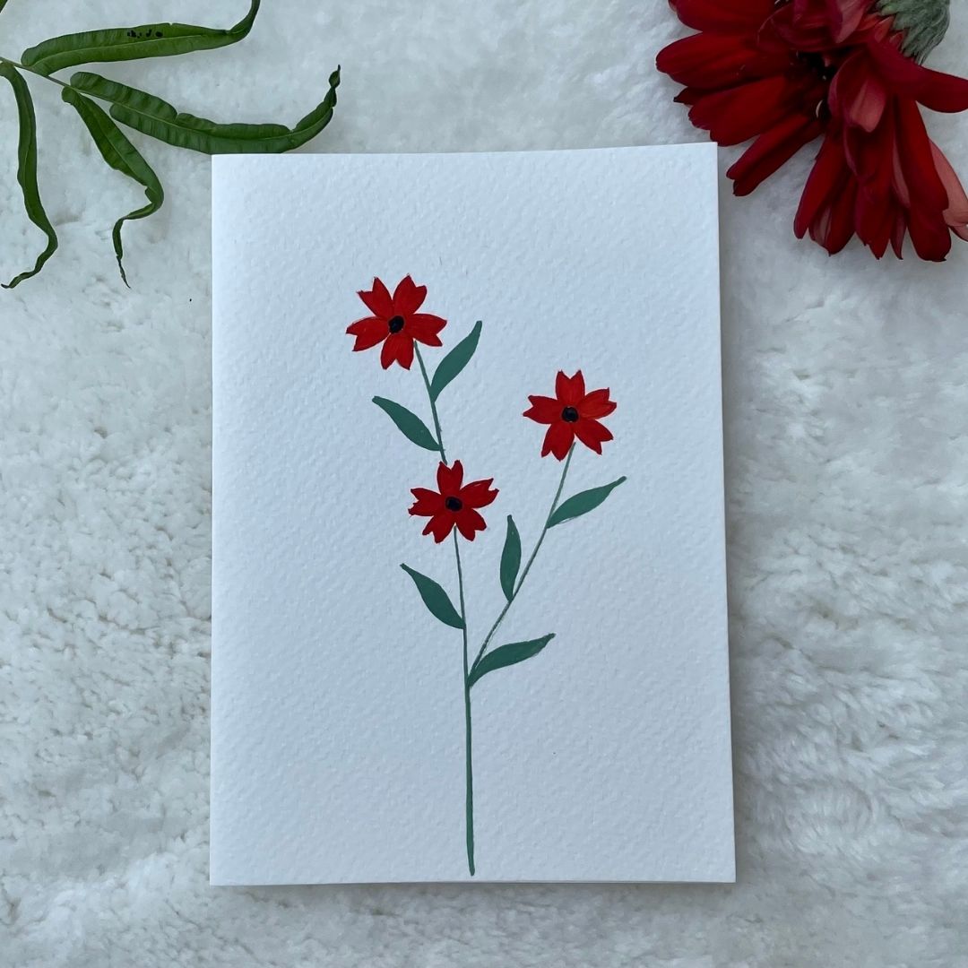 A hand-painted greeting card with red dogwood floral gouache illustration of small leaves on a white background, displayed on a fluffy surface with a small branch of leaves to the side.