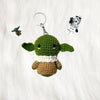 Crochet baby yoda keyring placed on a soft white fur fabric with a lego baby yoda and stromtrooper in the background