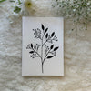Cherry blossom stalk in black hand painted on a greeting card placed on a soft white fabric with flowers in the background