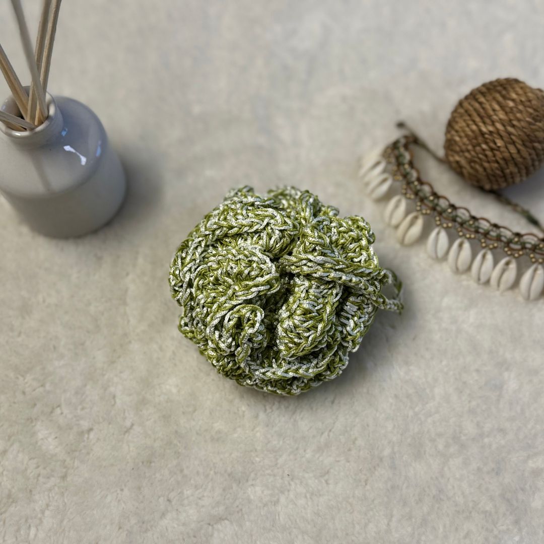 green crochet loofha placed on a soft white fabric with seashells and fragrance sticks in the background