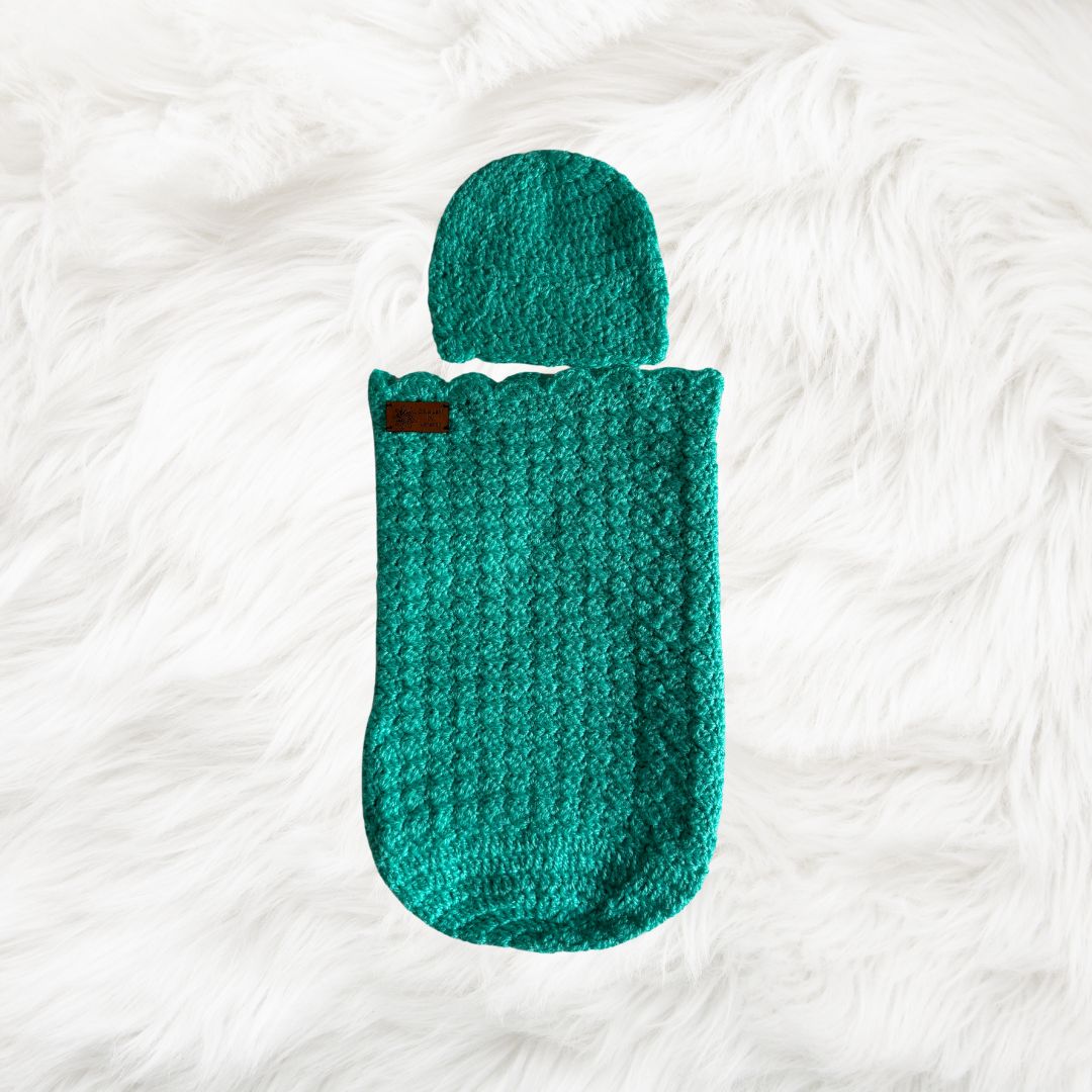 Green Crochet baby cocoon with a baby beanie placed on a white fur fabric