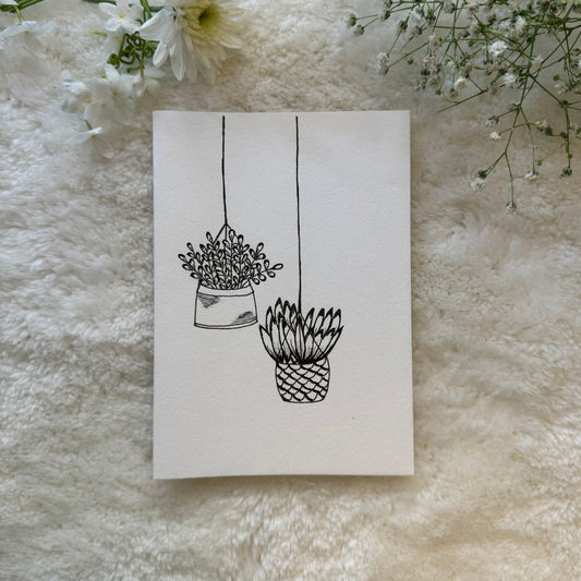 Black and white hanging pots hand draw on greeting card placed on a soft white cloth with flowers in the background