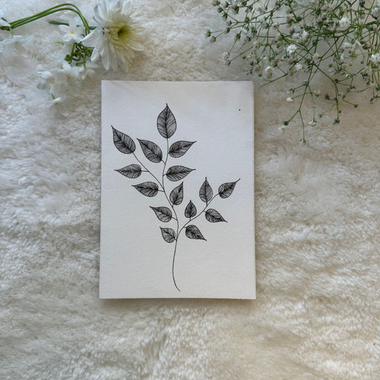 Hand drawn black and white line drawn leaves on a greeting card placed on a white soft cloth with flowers in the background