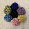 Different coloured hand crocheted loofhas arranged in a circle and placed on a soft white fabric