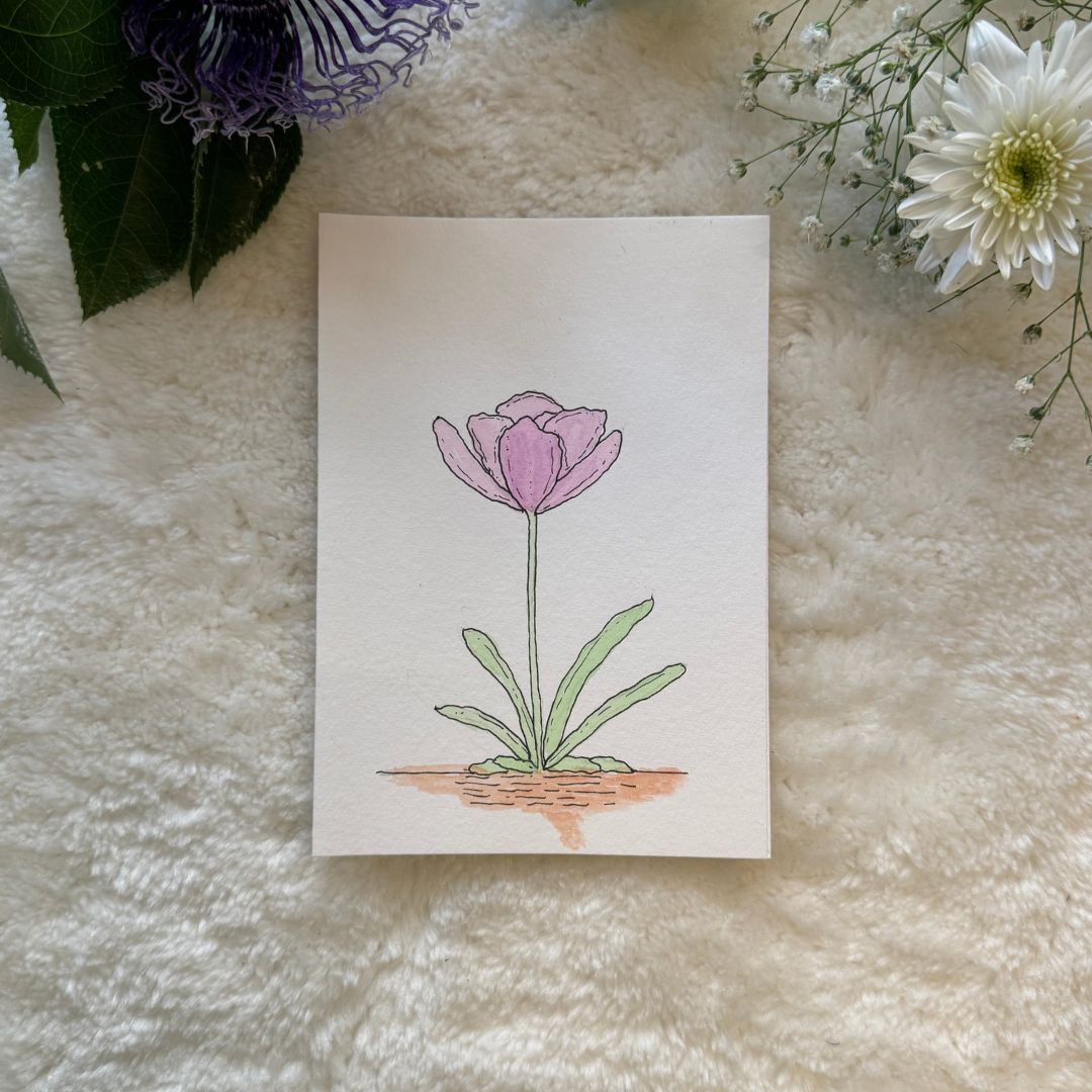 Pink lotus flower with green leaves painted on a greeting card placed on a soft white fabric with flowers in the background