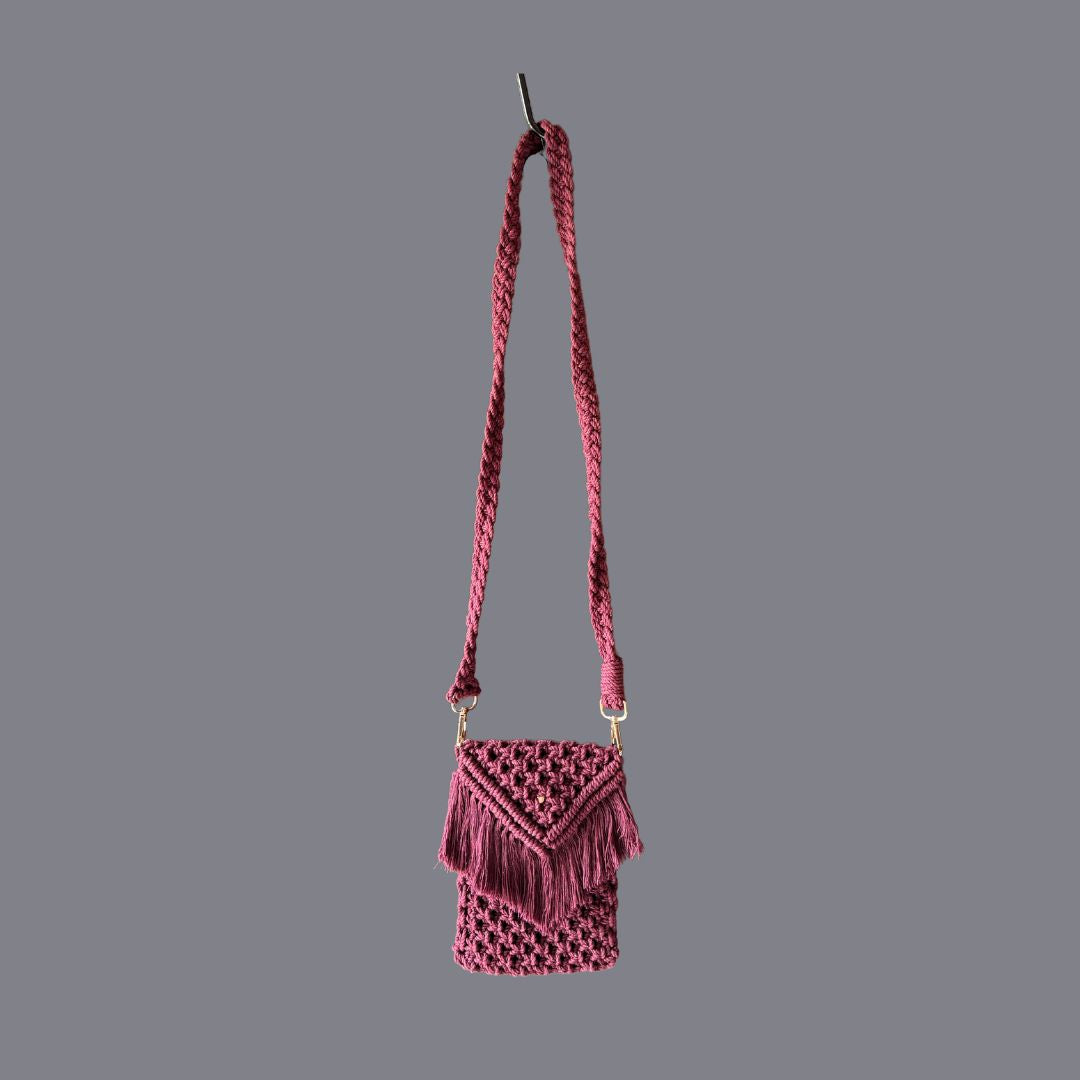 Maroon macrame small bag with a long handle placed against a grey background