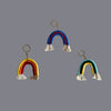 Trio coloured, rainbow shaped key ring done in macrame placed against a grey background