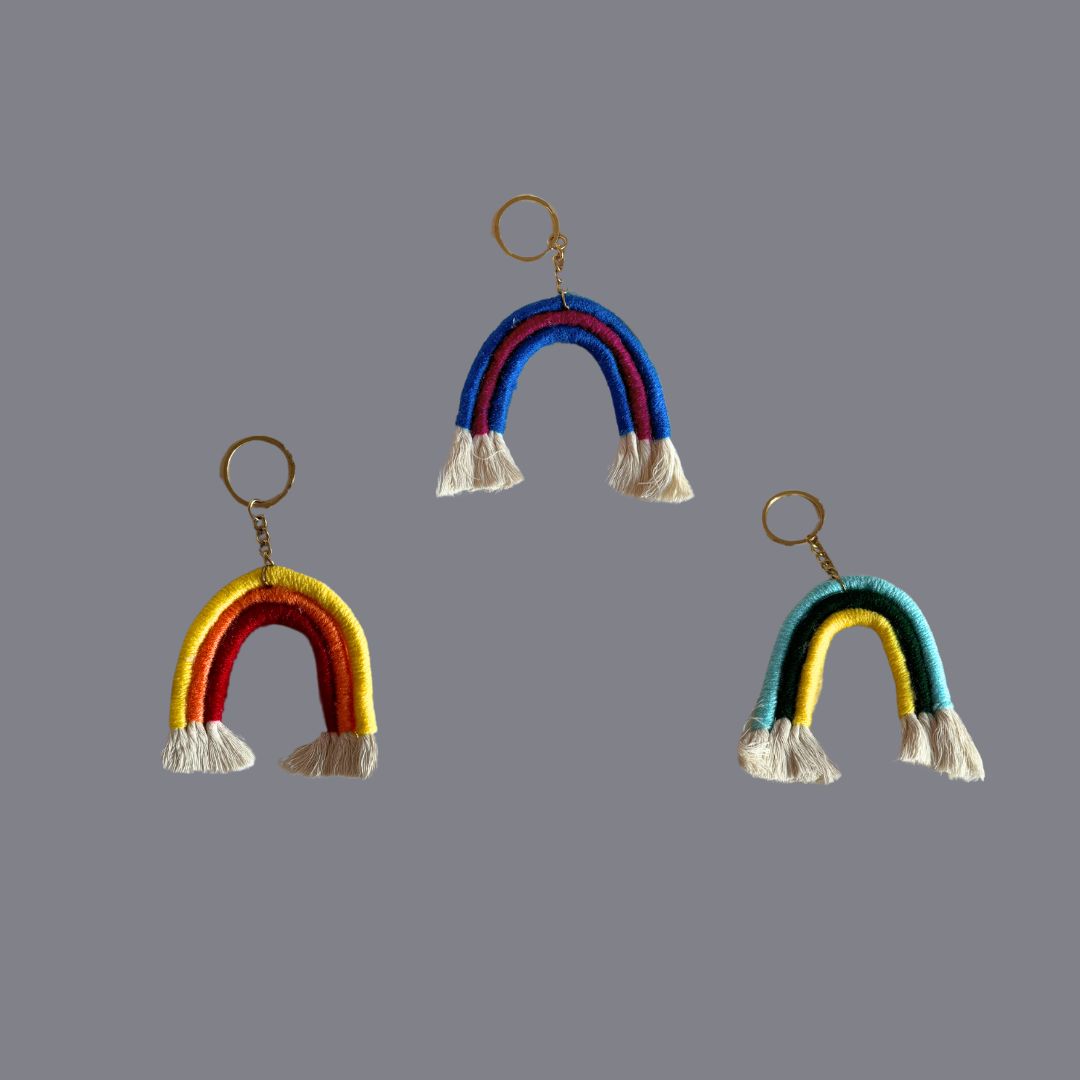 Trio coloured, rainbow shaped key ring done in macrame placed against a grey background
