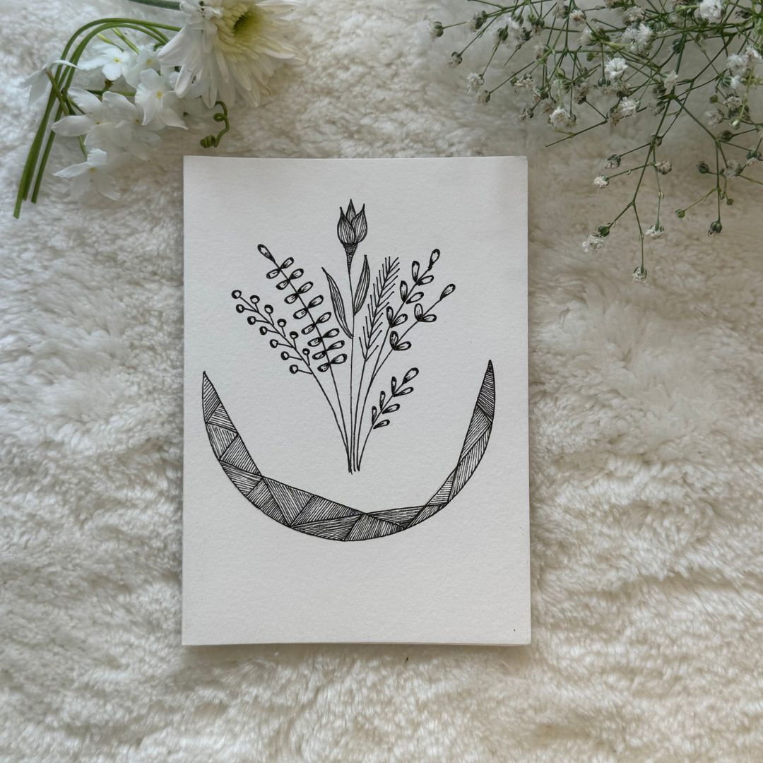 A hand-drawn black and white mandala art card placed on a white furry surface, with the card's design visible in the center.
