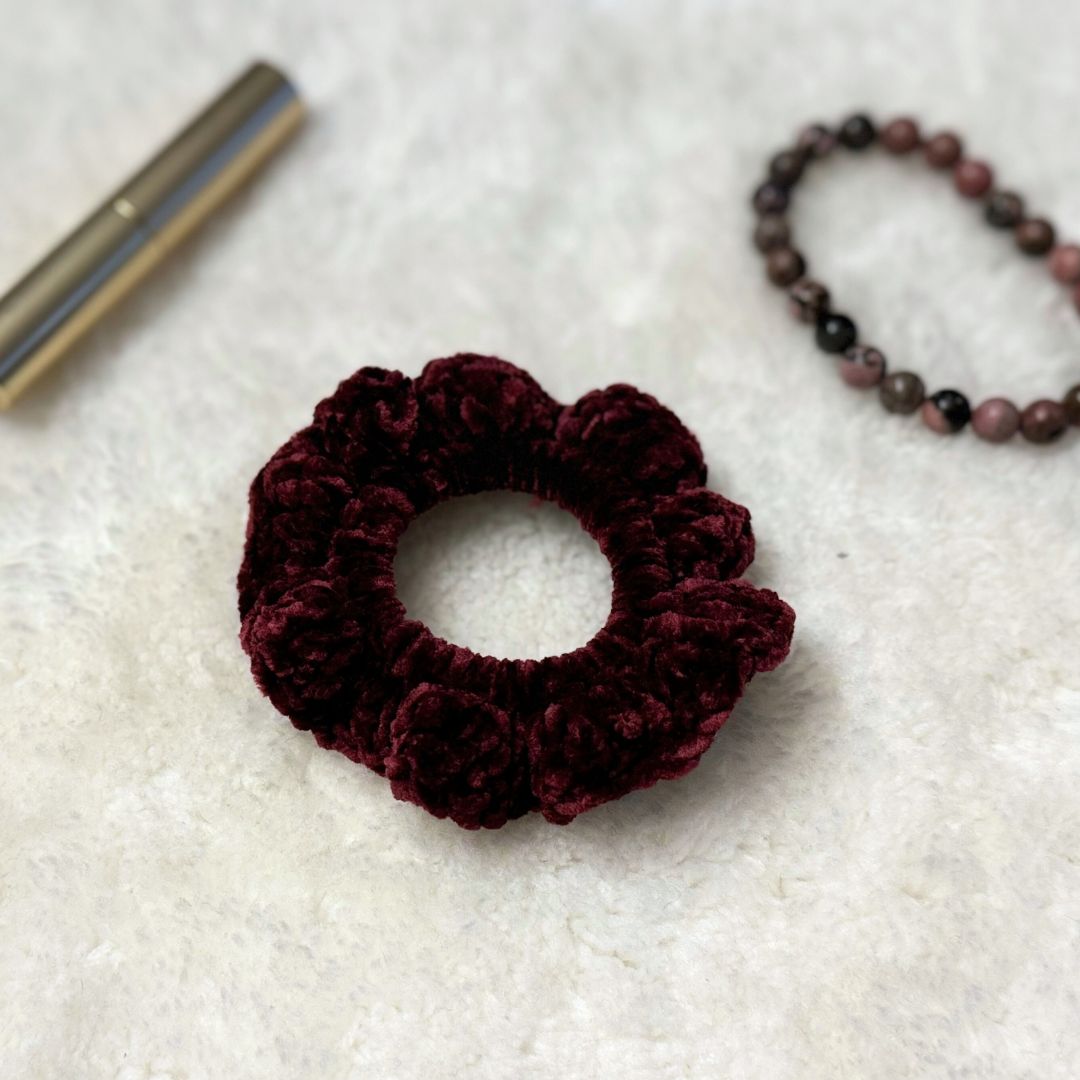 maroon velvet crochet scrunchie place on soft cloth with a lipstick and a bracelet in the background