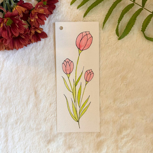 Watercolour Tulips painted on a bookmark placed on a white fur fabric with fresh flowers and leaves in the background