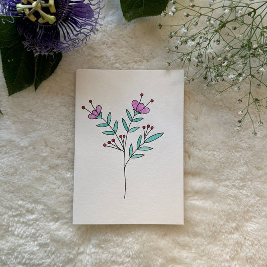 Pink flowers on a green stalk painted on a greeting card placed on a soft white fabric with flowers in the background