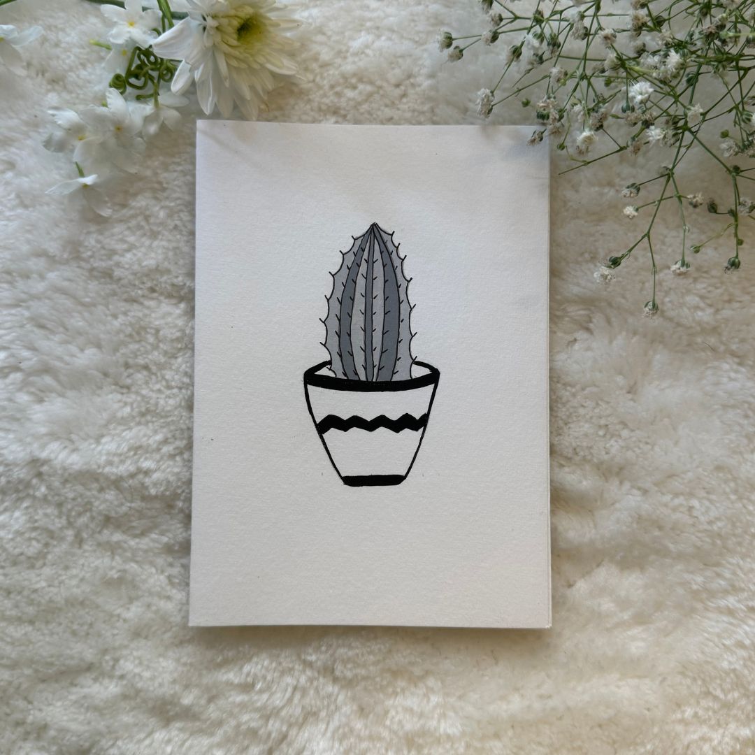 Black and white succulent pot hand painted on a greeting card placed on a soft fabric with flowers in the background