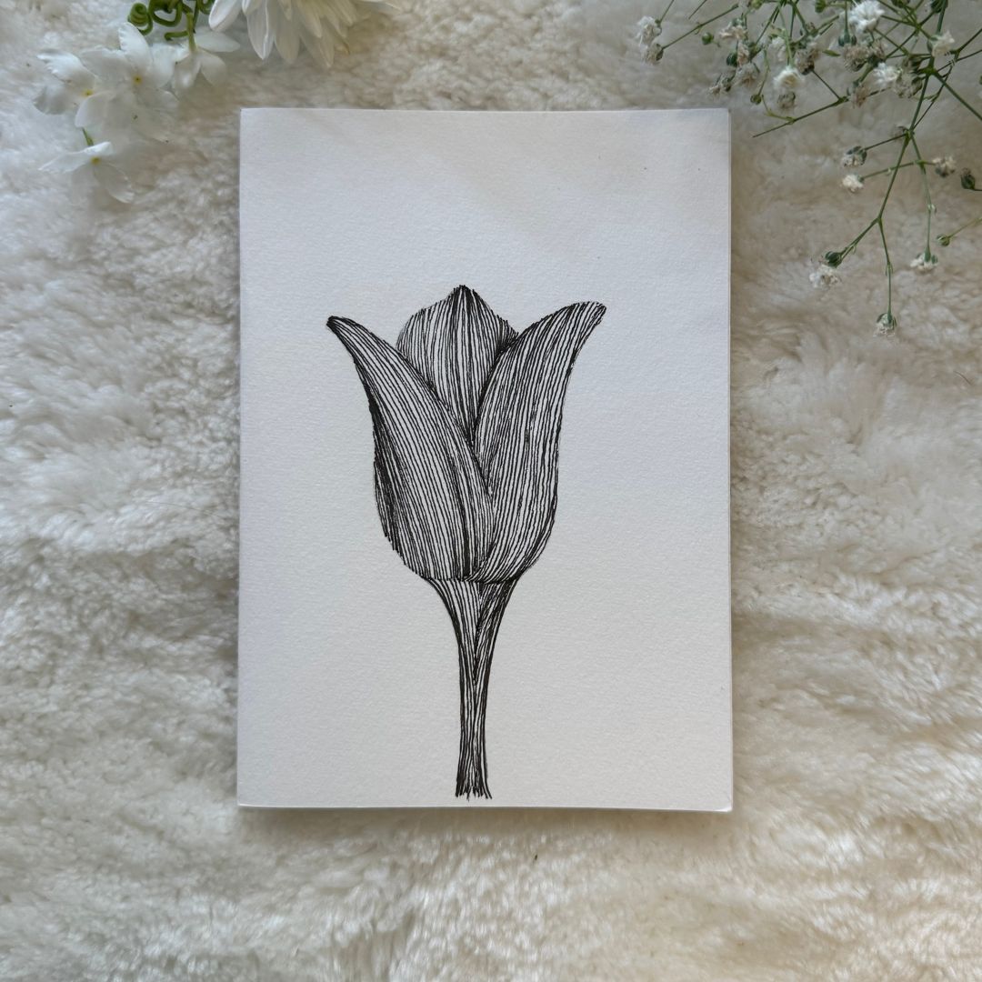 Black and white tulip hand drawn tulip on a card placed on a soft white fabric with flowers in the background