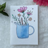 Blue watering can filed with flowers hand painted on a greeting card