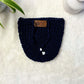 Black hand crocheted pot cozy with a drawstring and a faux leather olive leaf label placed on white fur fabric 