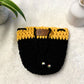 Yellow and Black hand crocheted pot cozy with a drawstring and a faux leather olive leaf label placed on white fur fabric 