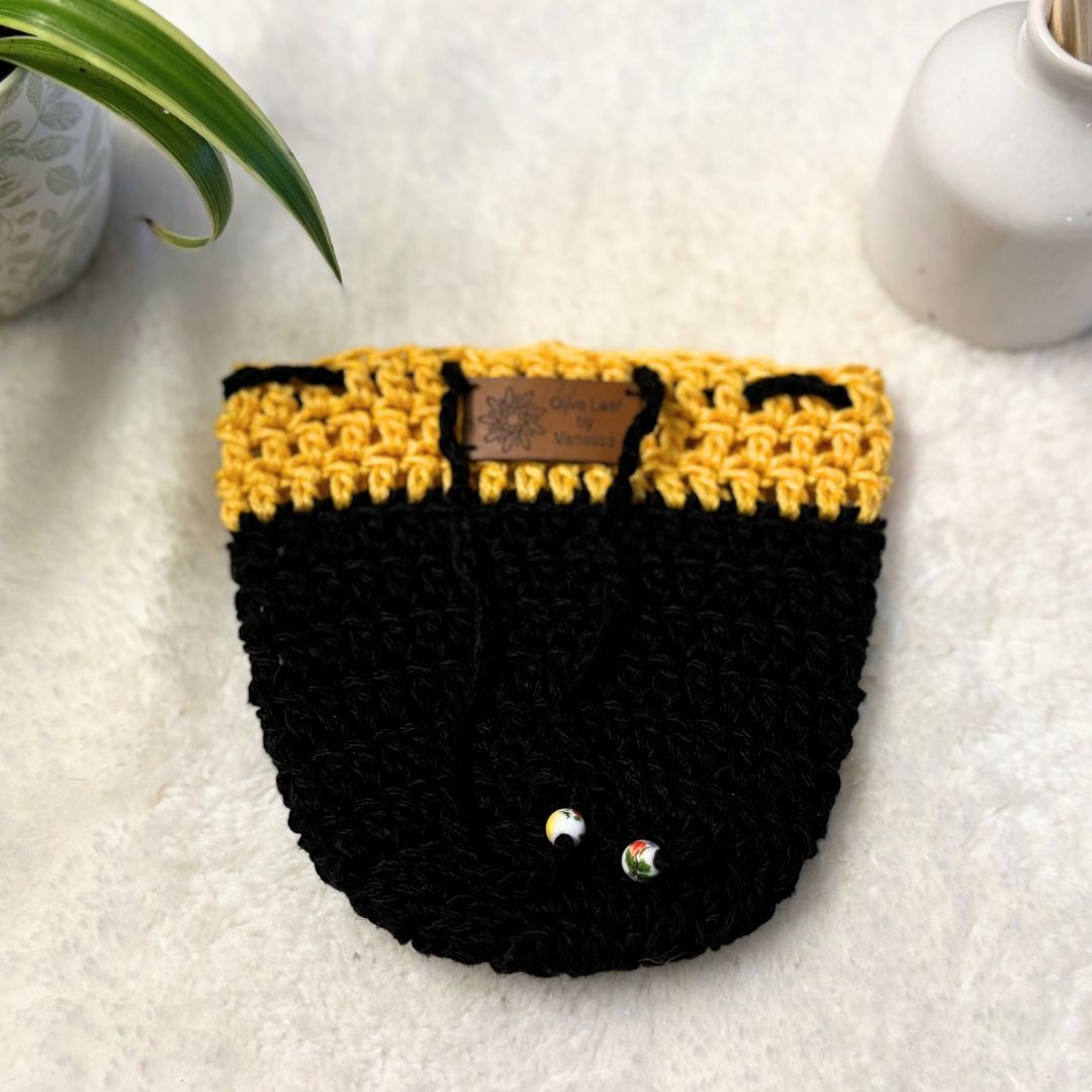 Yellow and Black hand crocheted pot cozy with a drawstring and a faux leather olive leaf label placed on white fur fabric 