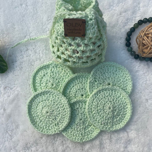A set of light green hand crocheted face scrubbies with a matching pouch, displayed on a soft surface.
