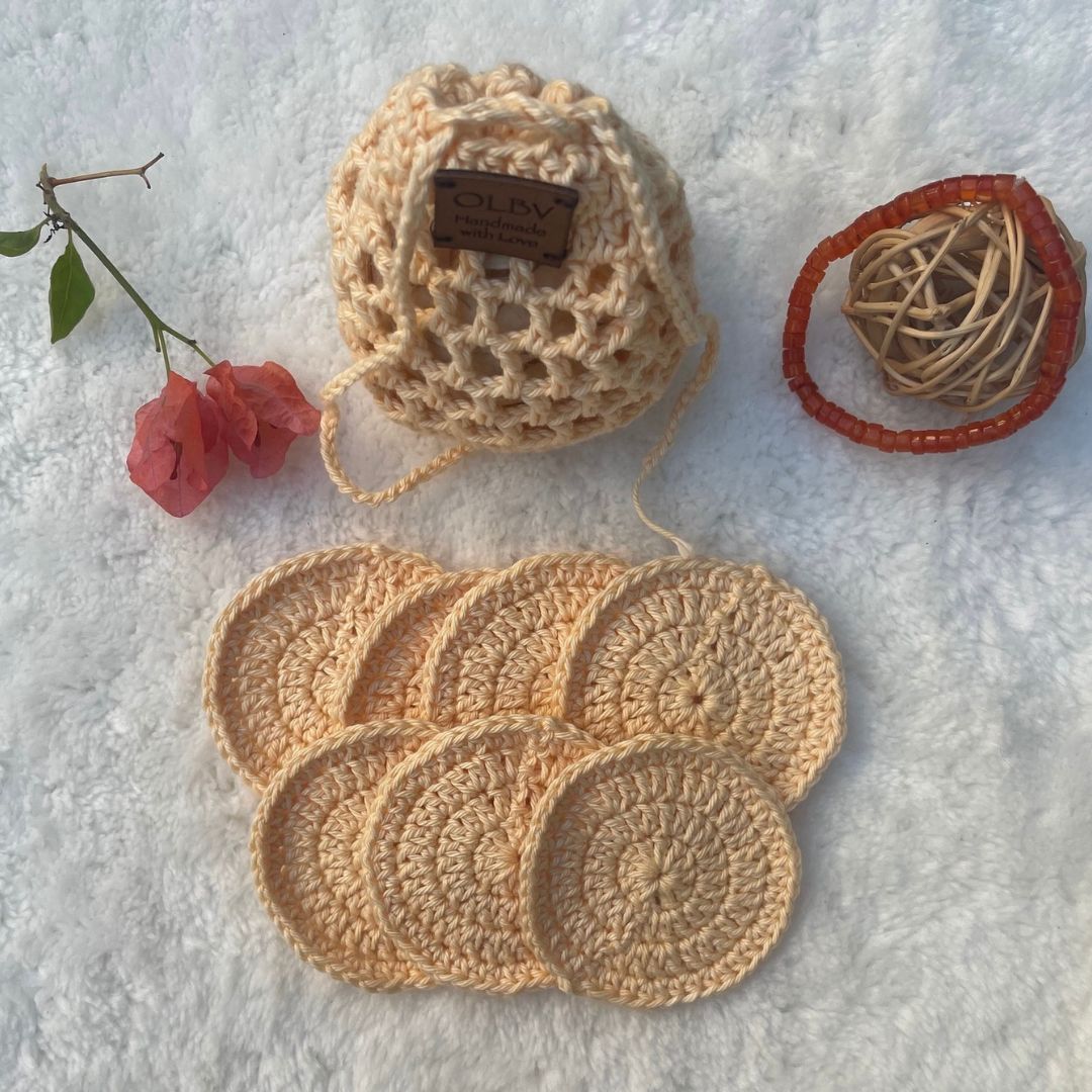 A set of peach hand crocheted face scrubbies with a matching pouch, displayed on a soft surface with light decor in the background 