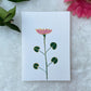 A hand painted greeting card with pink and gold lotus flower on white card stock placed on a fur surface.