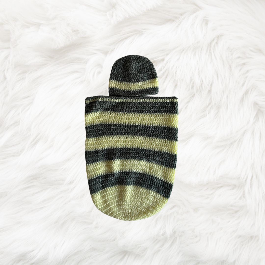 Yellow with grey stripes Crochet baby cocoon with a baby beanie placed on a white fur fabric