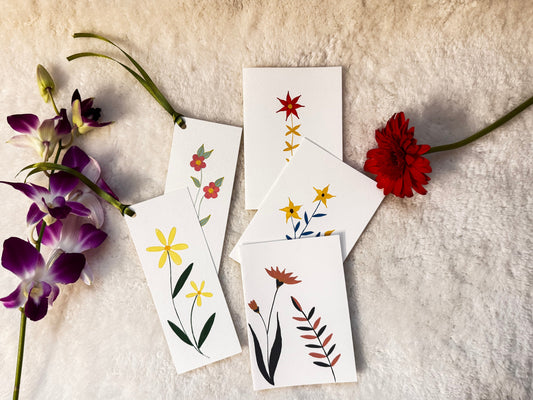 A set of white botanical art cards featuring hand-painted flowers and leaves, arranged on a textured cream fabric alongside purple orchids and a red flower.