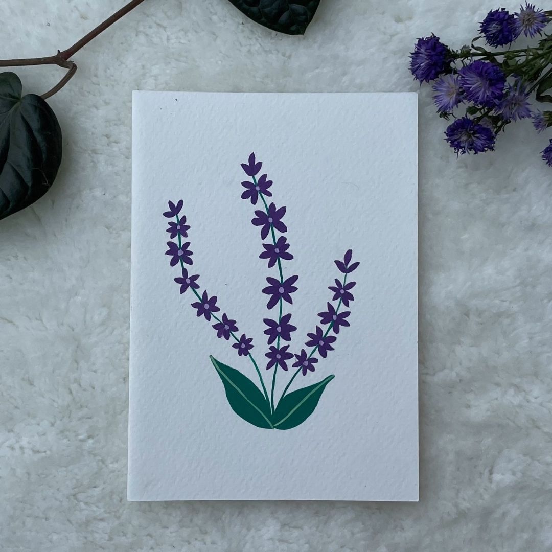 A hand painted greeting card with various flower stalks painted on a white card placed on a a fur cloth with decorative flowers in the background 