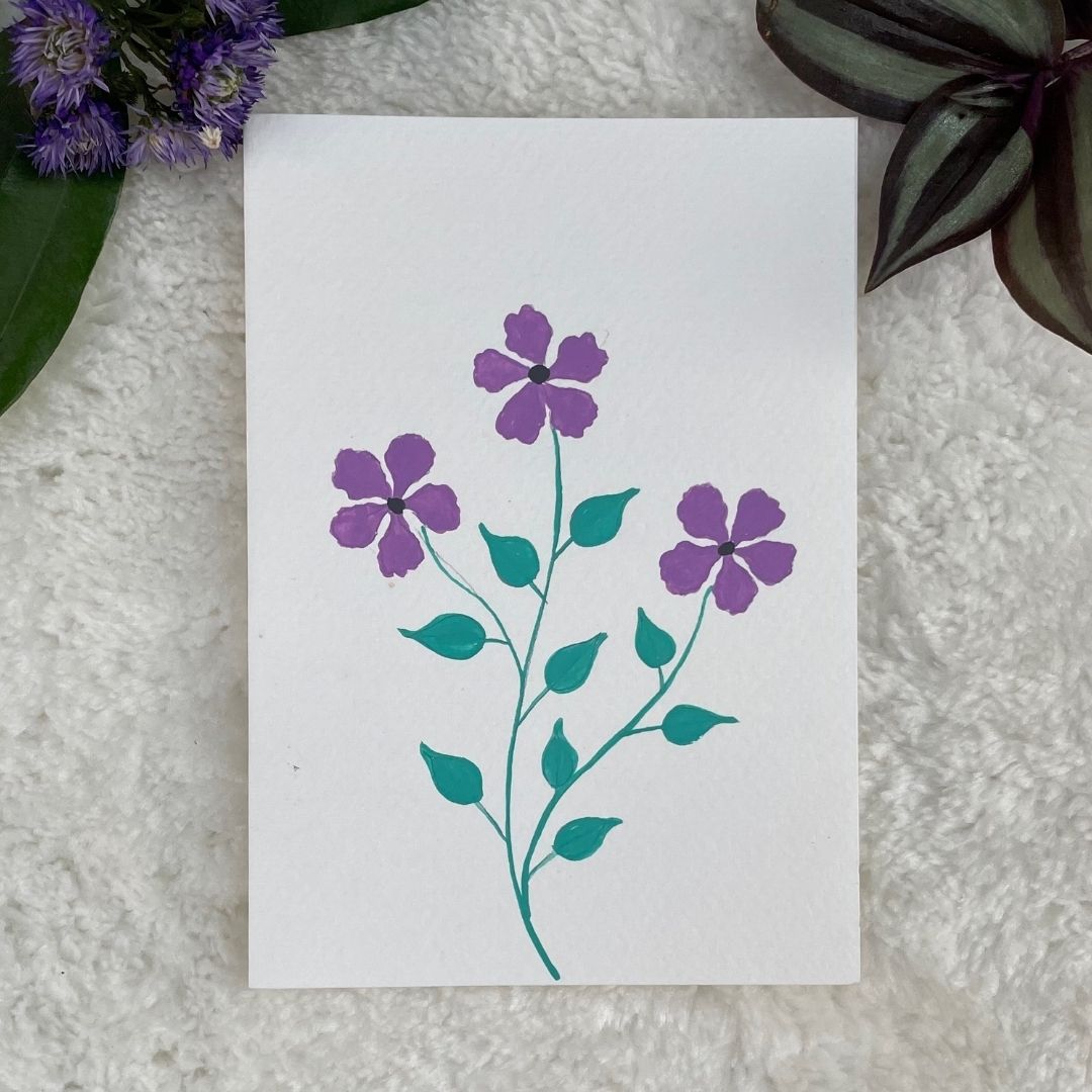 A hand painted greeting card with Purple flowers on a white card placed on a fur background 