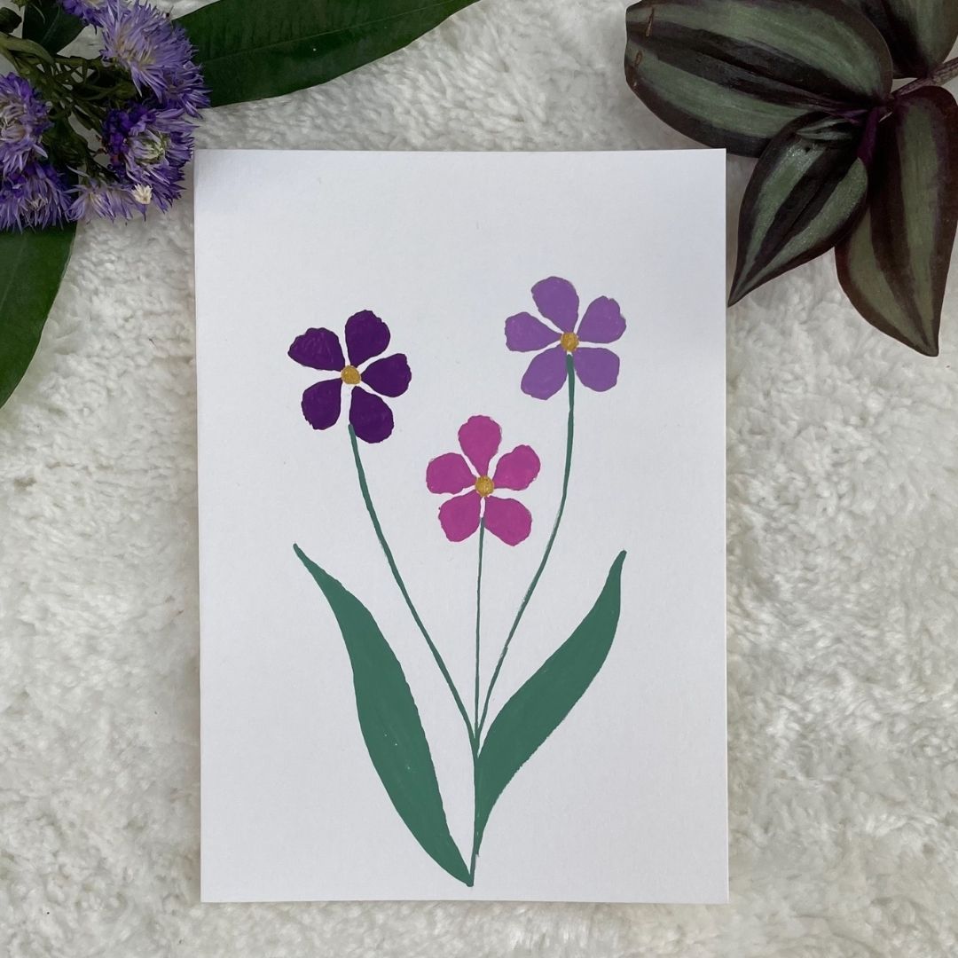 A hand painted greeting card with multi colour flowers on a white card placed on a fur background 