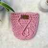 Pink hand crocheted pot cozy with a drawstring and a faux leather olive leaf label placed on white fur fabric 