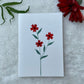 A hand-painted greeting card with red dogwood floral gouache illustration of small leaves on a white background, displayed on a fluffy surface with a small branch of leaves to the side.