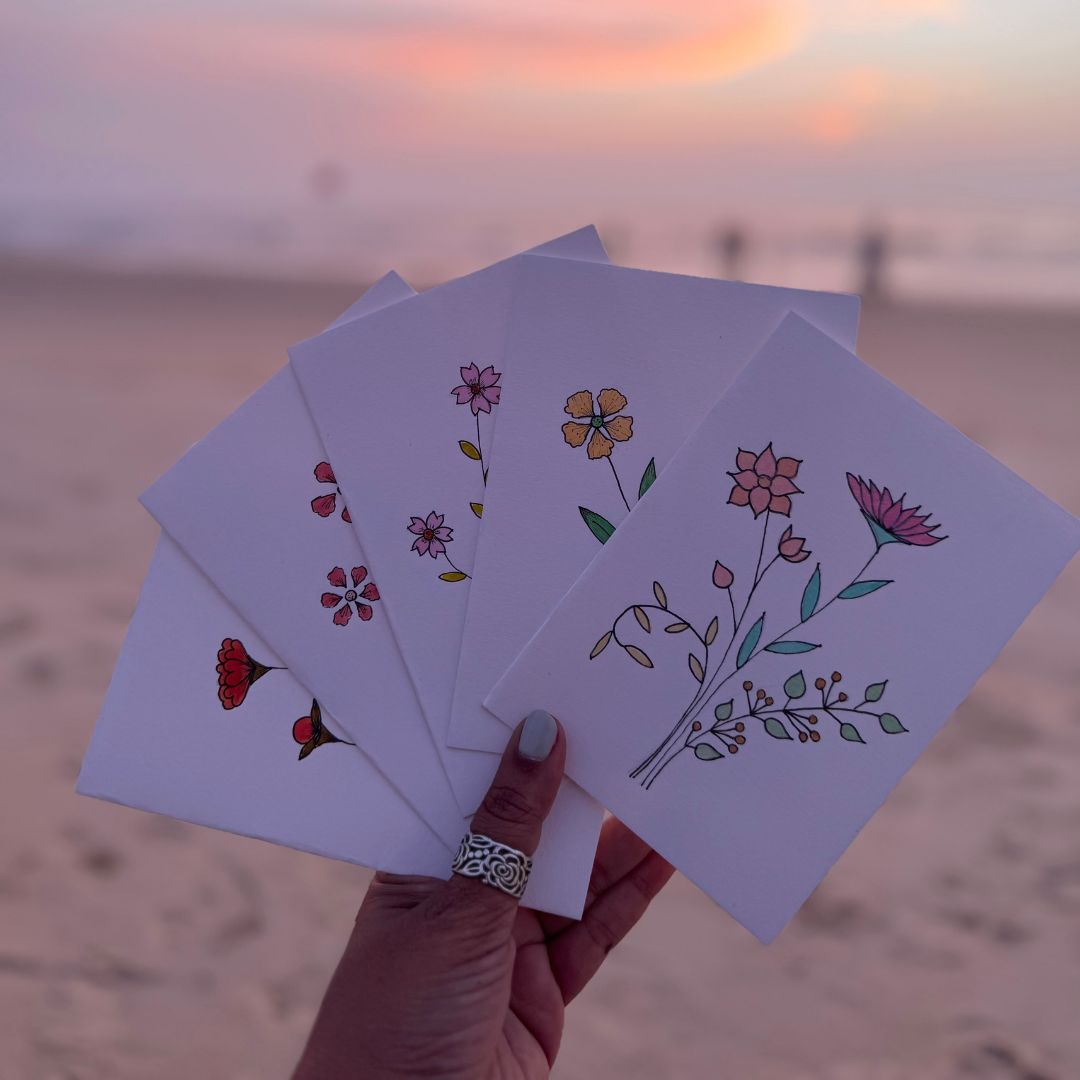 Hand holding floral cards with a sunset beach background