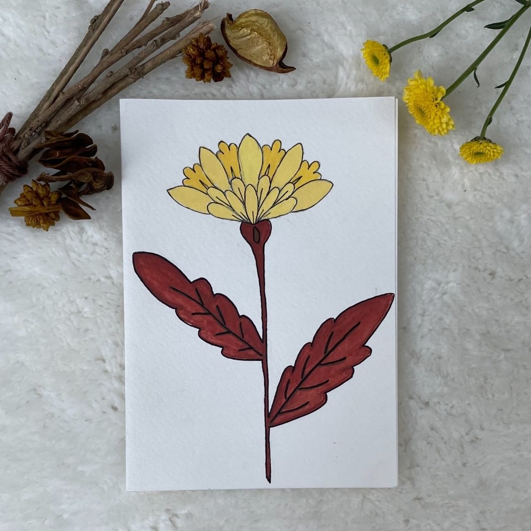 A hand painted greeting card with yellow flower stalks painted on a white card placed on a a fur cloth with decorative flowers in the background 