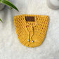 Yellow hand crocheted pot cozy with a drawstring and a faux leather olive leaf label placed on white fur fabric 