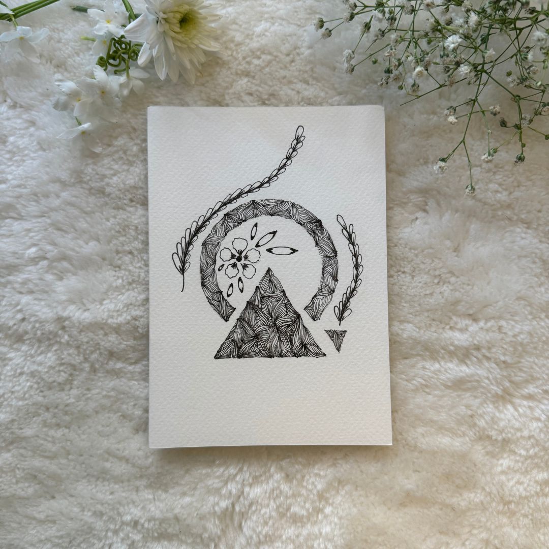 A hand-drawn black and white mandala art card placed on a white furry surface, with the card's design visible in the center.