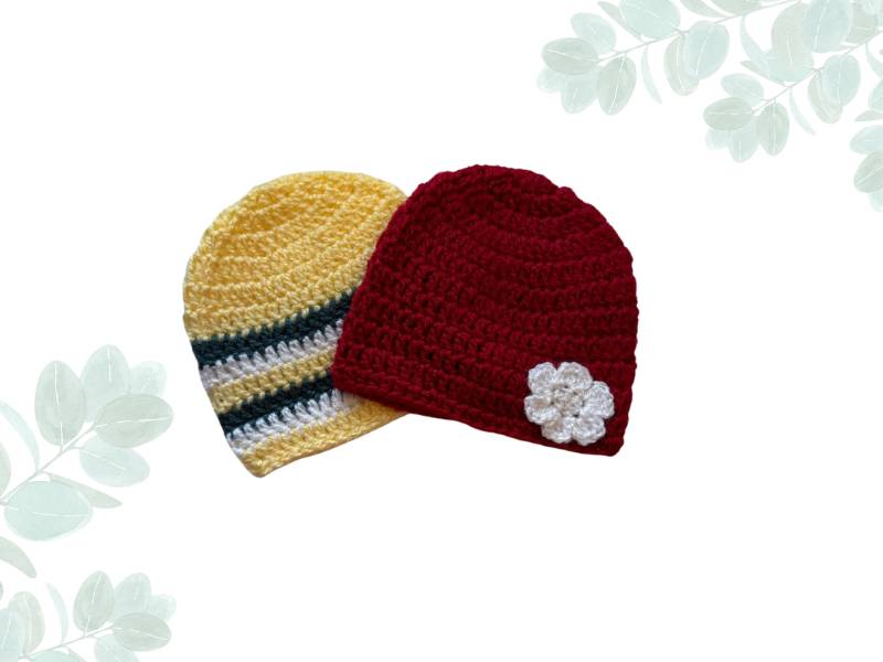 Two baby beanies- 1 yellow with grey stripes and the other red with a white flower placed on a white nature background 