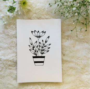 Black and white plant pt with a big flowed and leaves hand drawn on a card placed on a white background with flowers in the background 