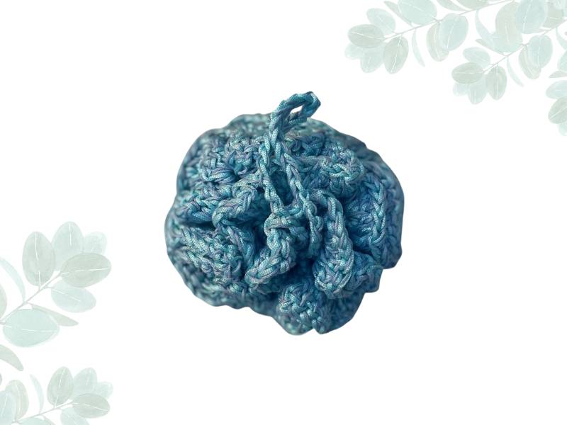 Blue hand crocheted loofha with a hang tie placed on a nature themed 
