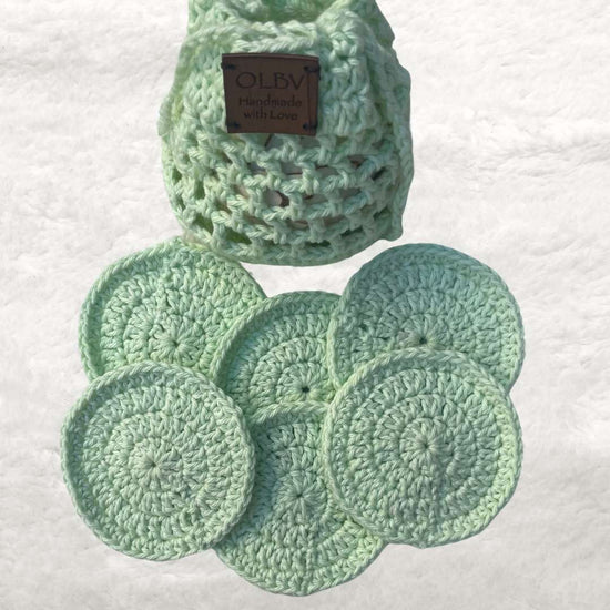 six crochet face scrubbies in light green placed in front of a crochet green pouch 