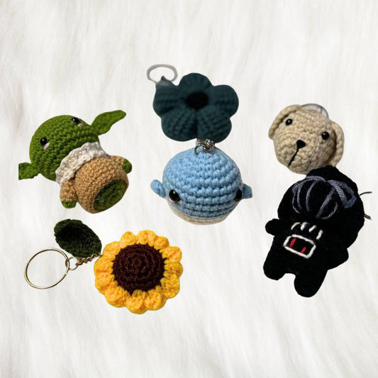 Plush crochet keyring baby yoda, darth vader inspired key ring, puppy face, sunflower a whale all spread out neatly on a white fur fabric 