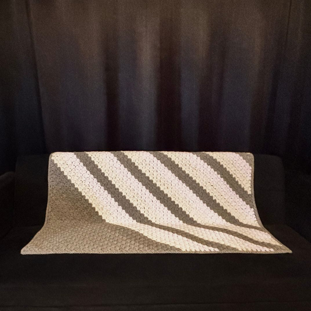 Chevron grey and purple sofa throw placed on a black sofa with black curtains in the background 