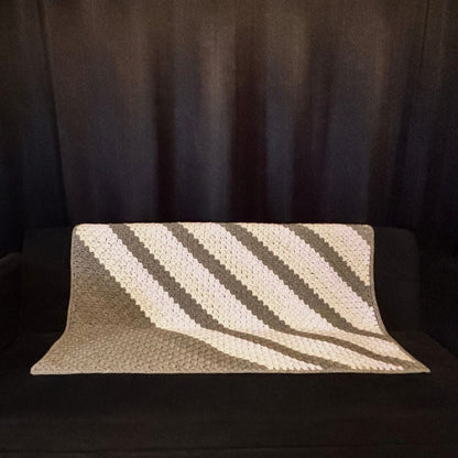 Chevron grey and purple sofa throw placed on a black sofa with black curtains in the background 