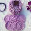 A set of purple hand crocheted face scrubbies with a matching pouch, displayed on a soft surface with decor in the background 