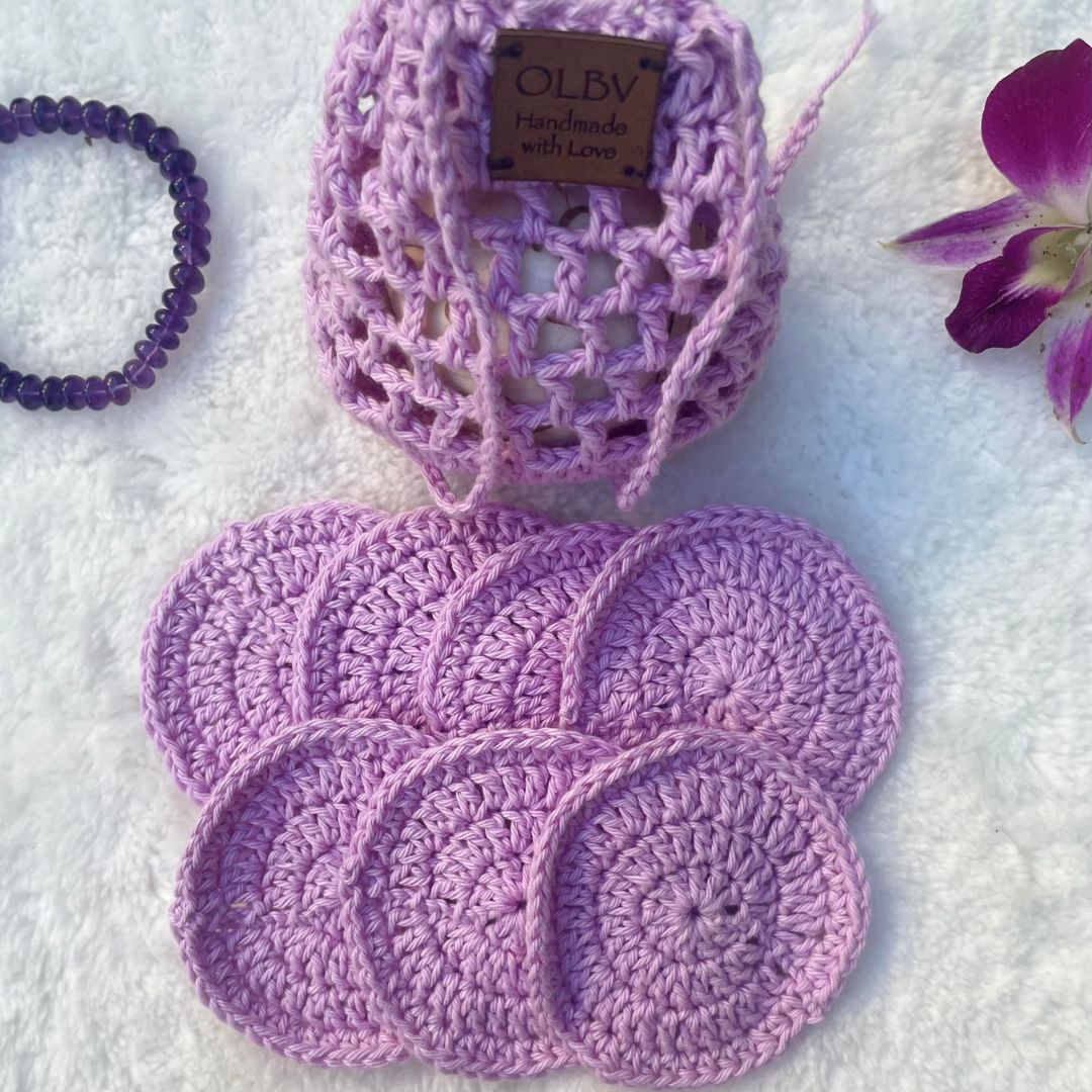 A set of purple hand crocheted face scrubbies with a matching pouch, displayed on a soft surface with decor in the background 