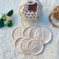A set of off white hand crocheted face scrubbies with a matching pouch, displayed on a soft surface.