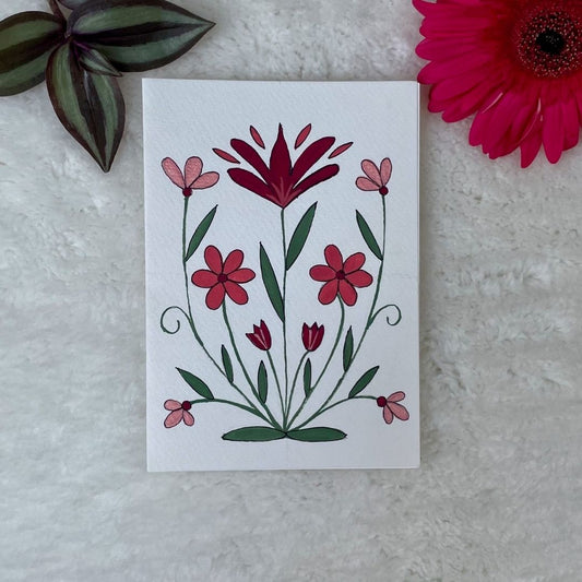 A hand painted greeting card with multi coloured flowers on a white card placed on a fur background 