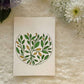 Abstract mandala filled with yellow and green leaves painted on a card, place on a white background with fresh flowers 