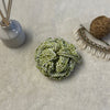 green crochet loofha placed on a soft white fabric with seashells and fragrance sticks in the background